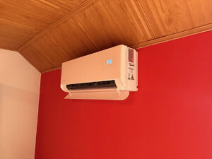 Vnitřní jednotka Midea Breezeless E na stěně místnosti s červenou omítkou a dřevěným podhledem, instalace klimatizace BCE